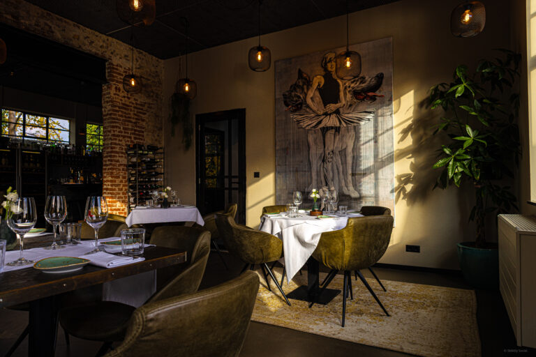 Sfeervolle restaurant eetzaal met gedekte tafels, olijfgroene stoelen en kunstwerk, badend in zonlicht.