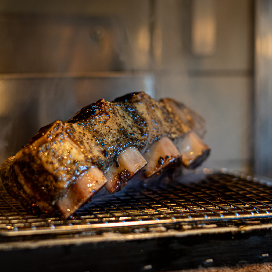 Gegrilde, gekruide ribben met een glimmende korst roken op een metalen rooster in een oven.
