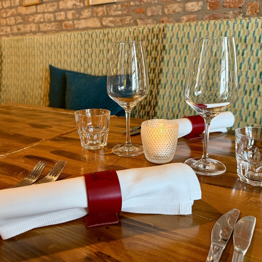 Restauranttafel gedekt met bestek, glazen, servetten en kaarsen.