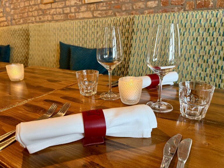 Restauranttafel gedekt met bestek, glazen, servetten en kaarsen.