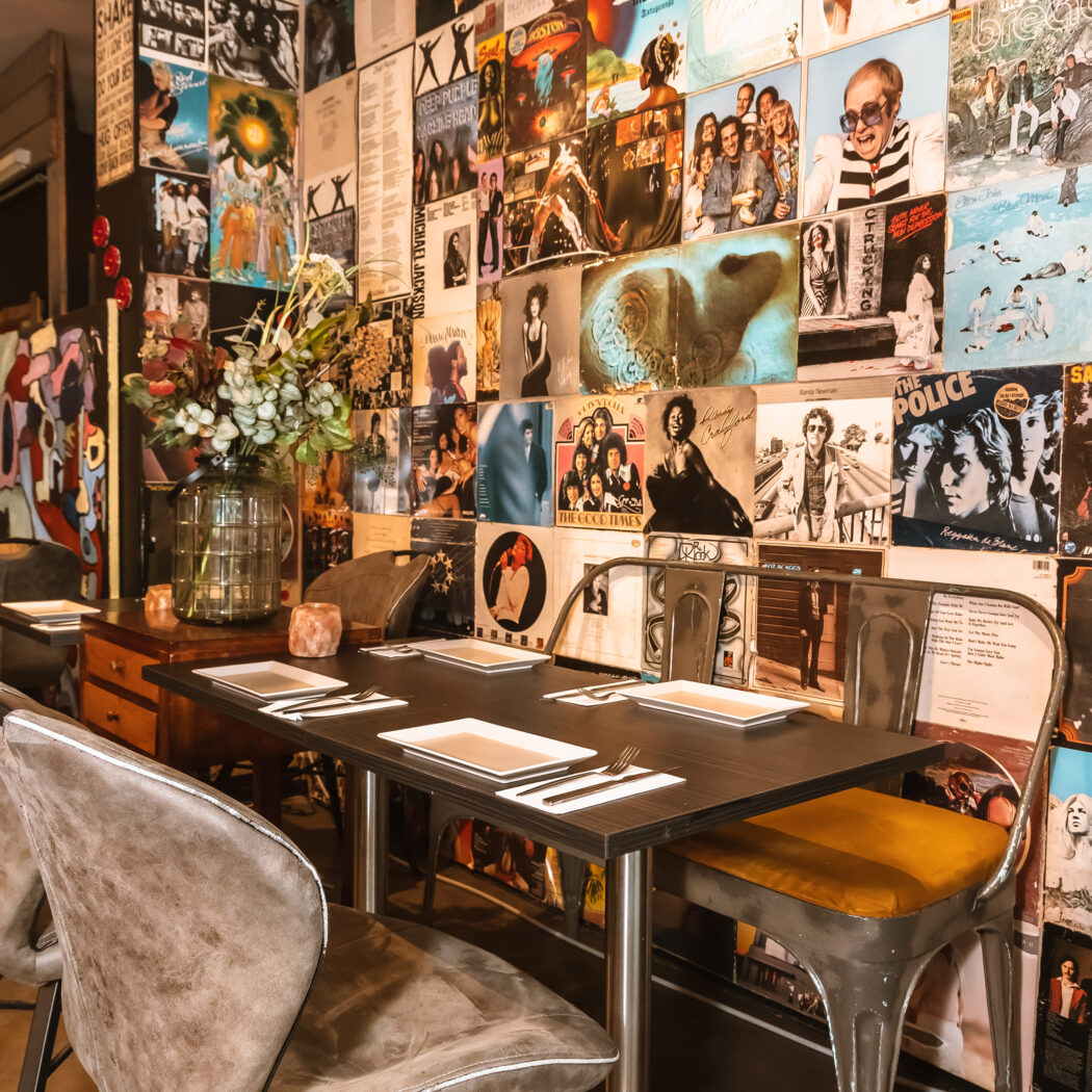 Restaurant met muren vol iconische vinylplatenhoezen en een gedekte tafel met grijs gestoffeerde stoelen.