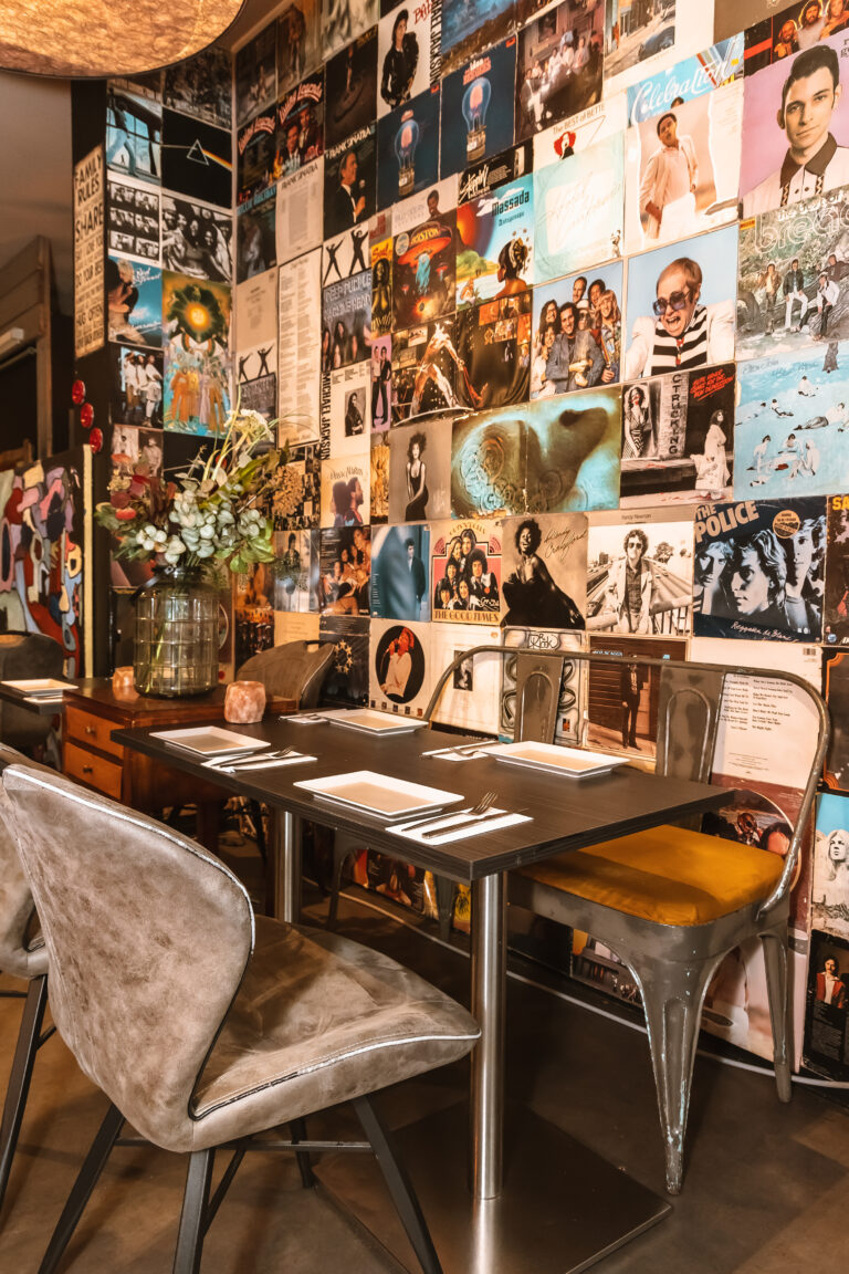 Restaurant met muren vol iconische vinylplatenhoezen en een gedekte tafel met grijs gestoffeerde stoelen.