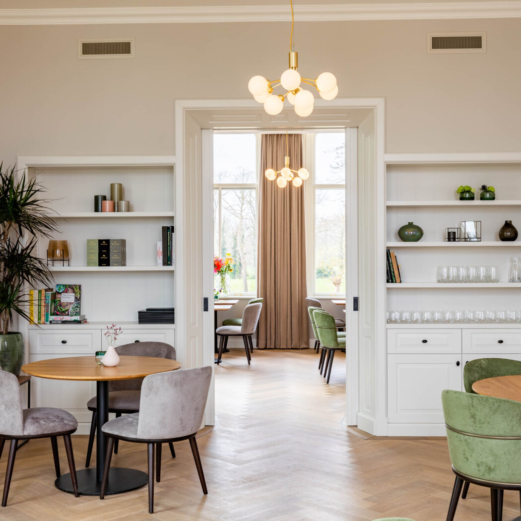 Licht en modern restaurant interieur met visgraatparket, gezellige zitjes, en witte inbouwkasten.