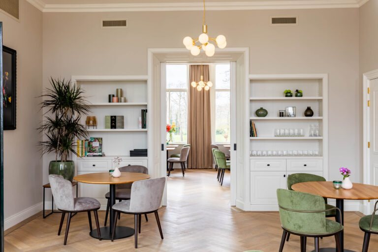 Licht en modern restaurant interieur met visgraatparket, gezellige zitjes, en witte inbouwkasten.