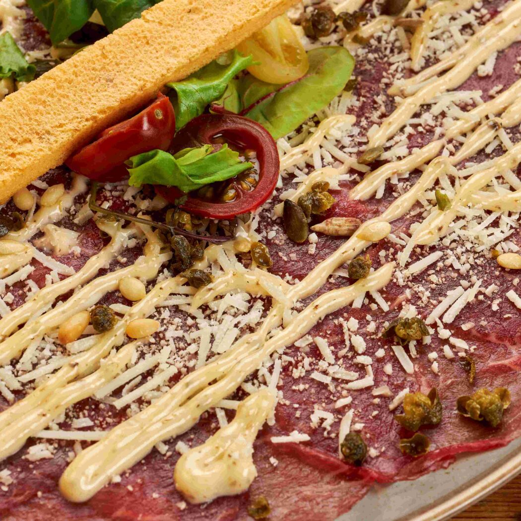 Runder carpaccio met truffelmayonaise, Parmezaanse kaas, pijnboompitten, kappertjes, salade en een broodstengel.