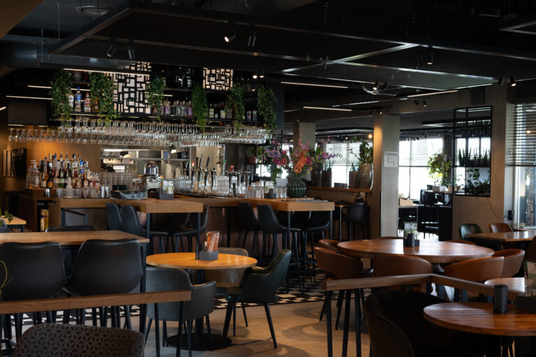 Sfeervol restaurantinterieur met een goed gevulde bar, houten tafels en comfortabele zwarte stoelen.