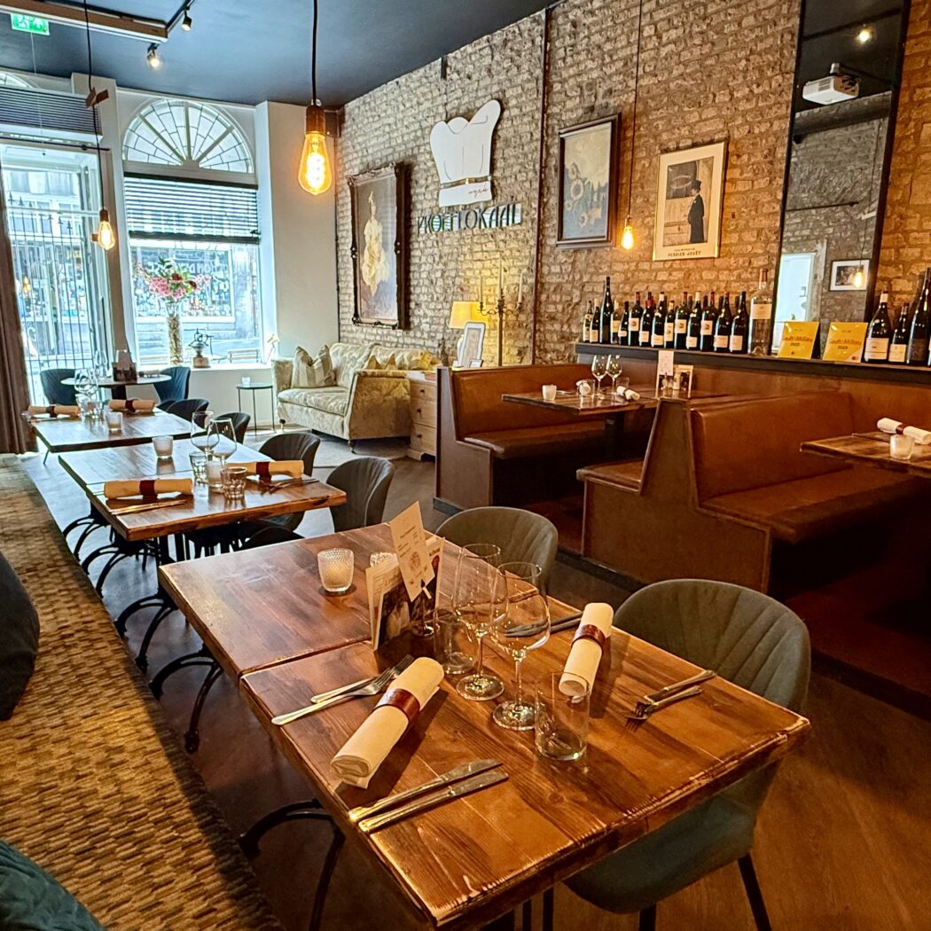 Restaurantinterieur: houten tafels, lederen banken,  wijnrek en wanddecoratie.