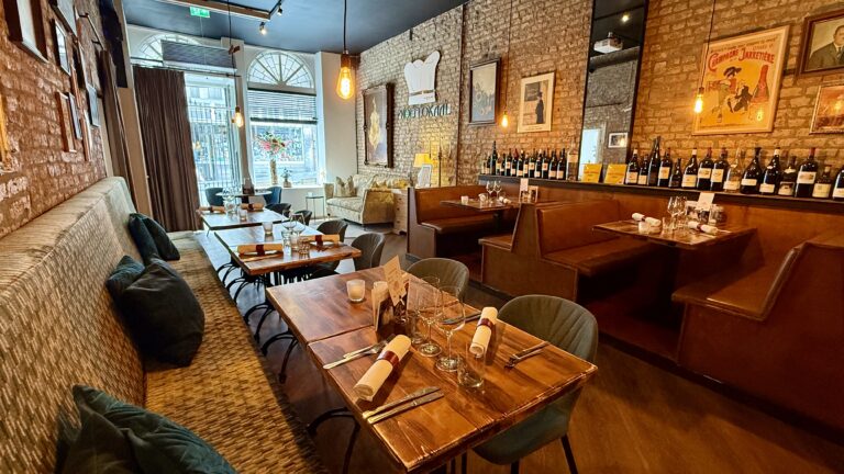 Restaurantinterieur: houten tafels, lederen banken,  wijnrek en wanddecoratie.