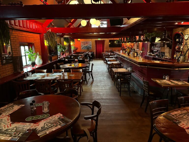 Sfeervol restaurant met donkere houten tafels, rode bakstenen muren, een lange bar en hangplanten.