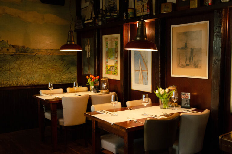 Twee gedekte tafels in een gezellig restaurant met een Hollands polderlandschap als muurschildering en warme lampen.