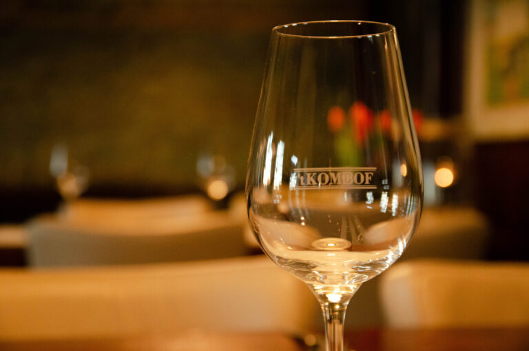 Leeg wijnglas met het logo t KOMBÔF in een sfeervol restaurant.