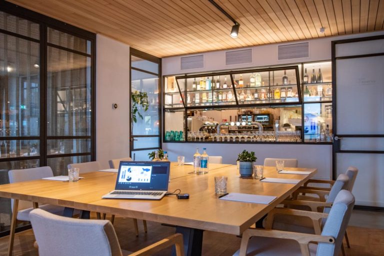 Stijlvolle vergaderruimte met houten tafel, laptop die een presentatie toont, en een bar achter glas.