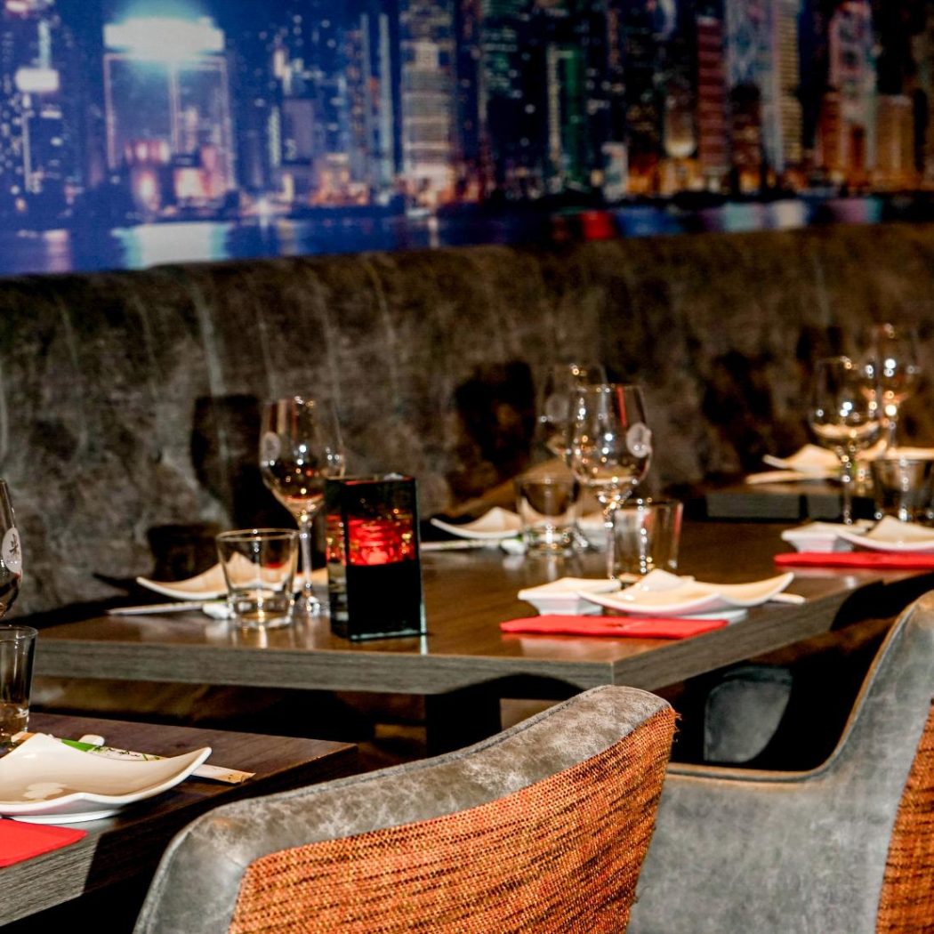 Stijlvol restaurantinterieur met gedekte tafels, rode servetten en een verlichte stadsgezicht muur.