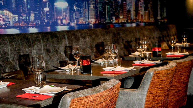 Stijlvol restaurantinterieur met gedekte tafels, rode servetten en een verlichte stadsgezicht muur.