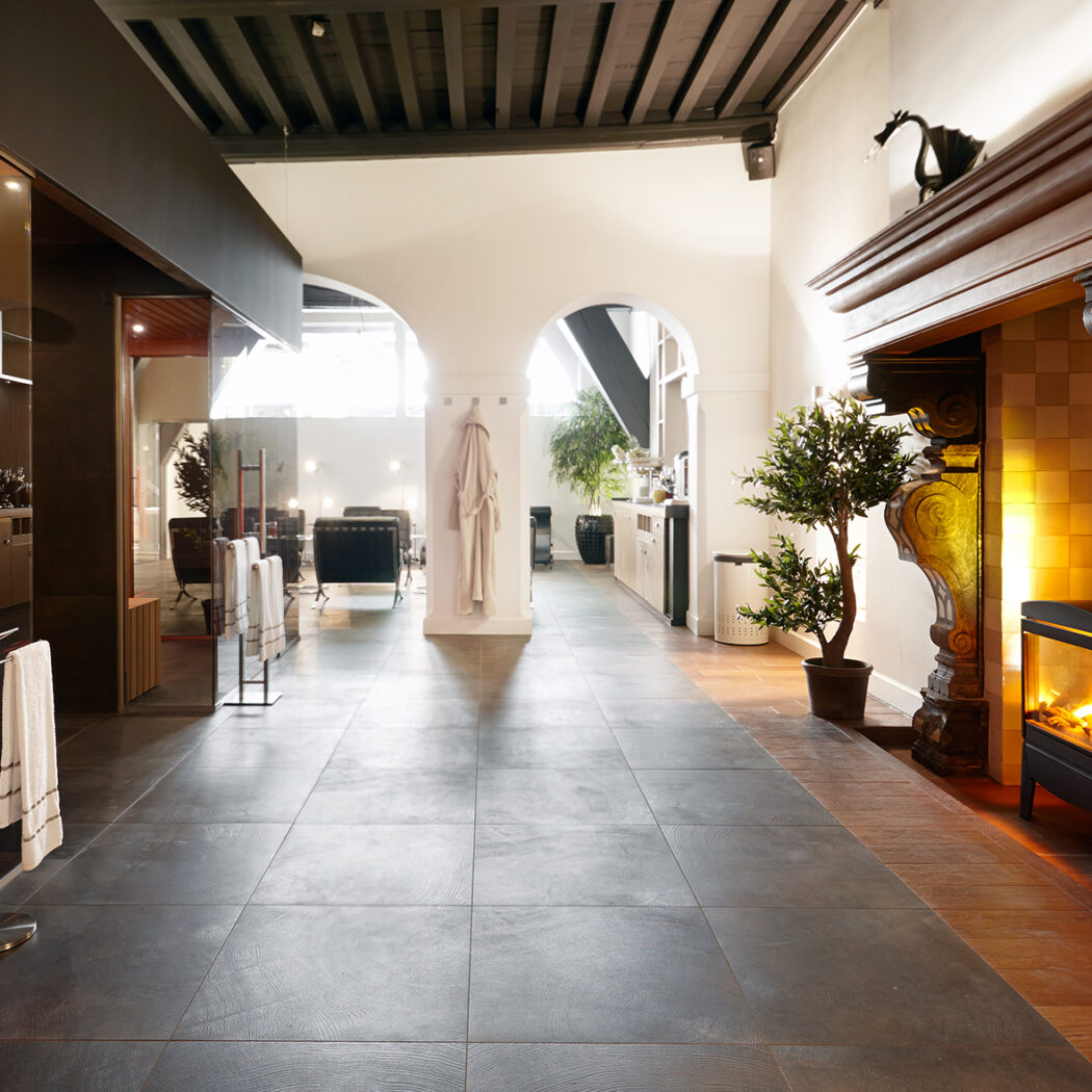 Ruime wellnessruimte met sauna, klassieke schouw, donkere tegelvloer en houten balkenplafond.