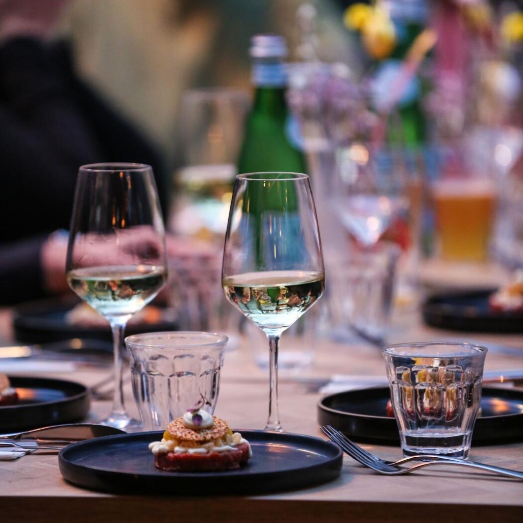 Dichtbij shot van een gedekte eettafel met witte wijn, een amuse op een zwart bord en een San Pellegrino fles.