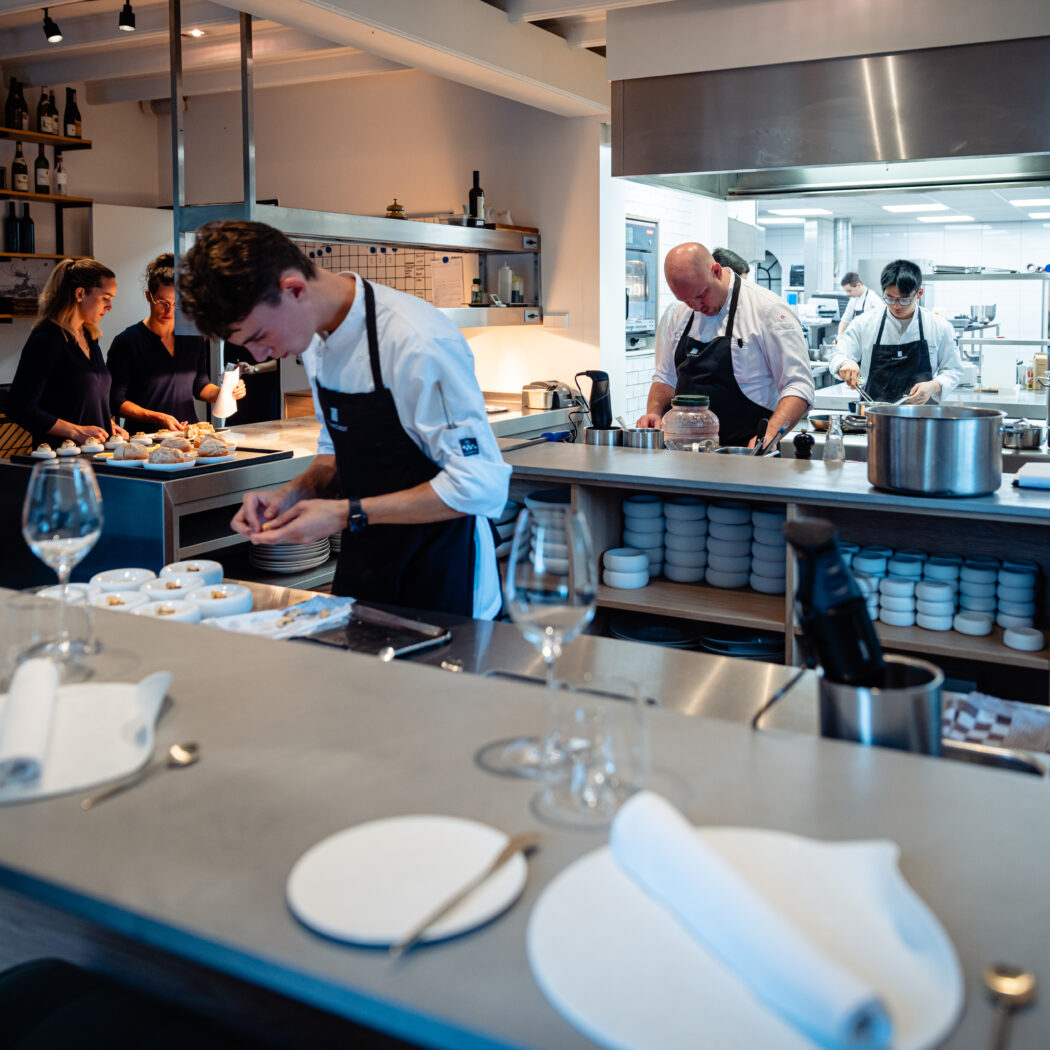 Meerdere koks bereiden en schikken gerechten in een strakke, open restaurantkeuken, met opgemaakte borden in de voorgrond.