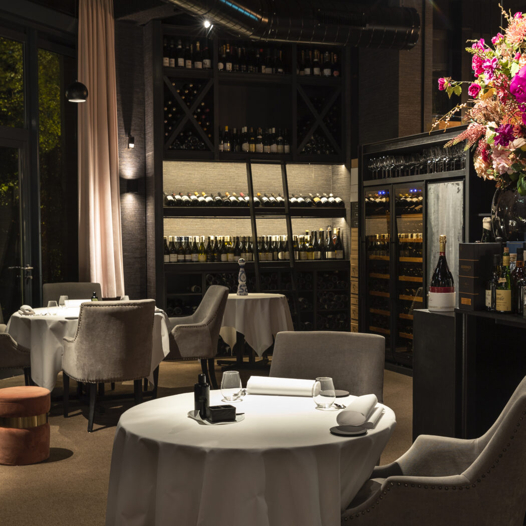 Sfeervol restaurant met gedekte tafels, een uitgebreide wijncollectie en een groot bloemstuk.