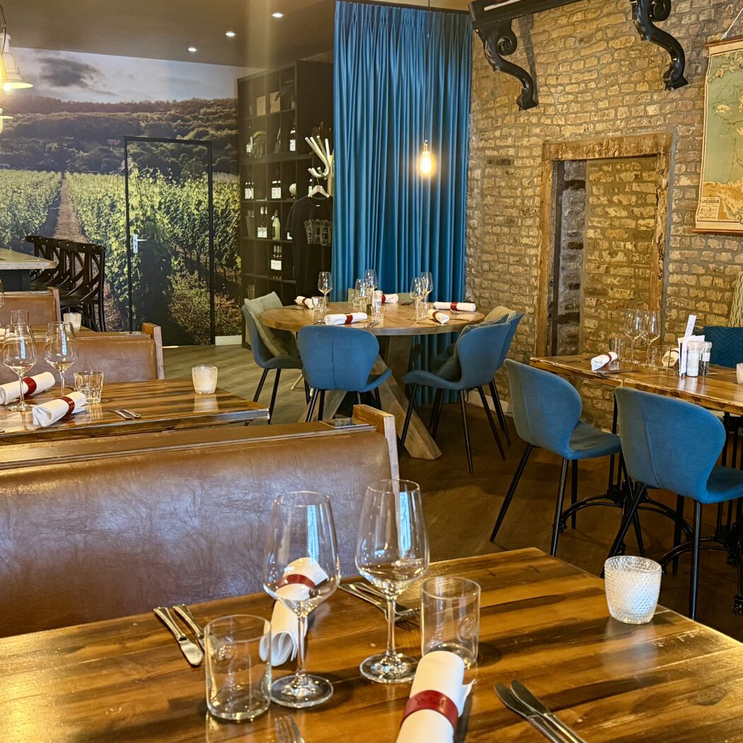 Restaurant interieur: houten tafels, blauwe stoelen, wijngaardmuurschildering.