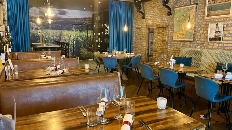 Restaurant interieur: houten tafels, blauwe stoelen, wijngaardmuurschildering.