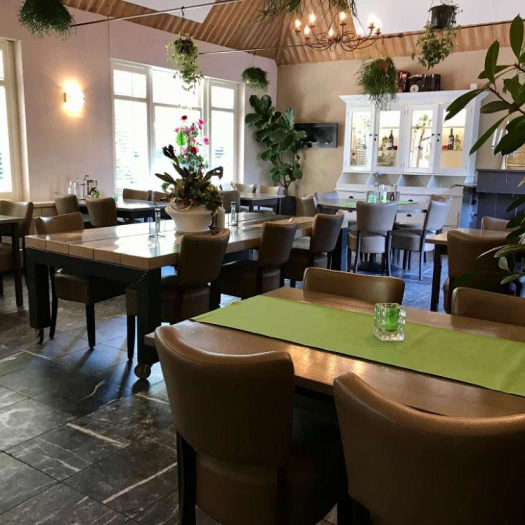 Sfeervolle, lichte restaurantruimte met houten tafels, groene lopers en bruine stoelen, inclusief tafelnummer 18.