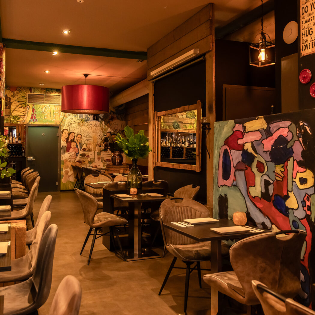 Sfeervol restaurantinterieur met eclectische kunst aan de muren, ingerichte tafels en warme verlichting.