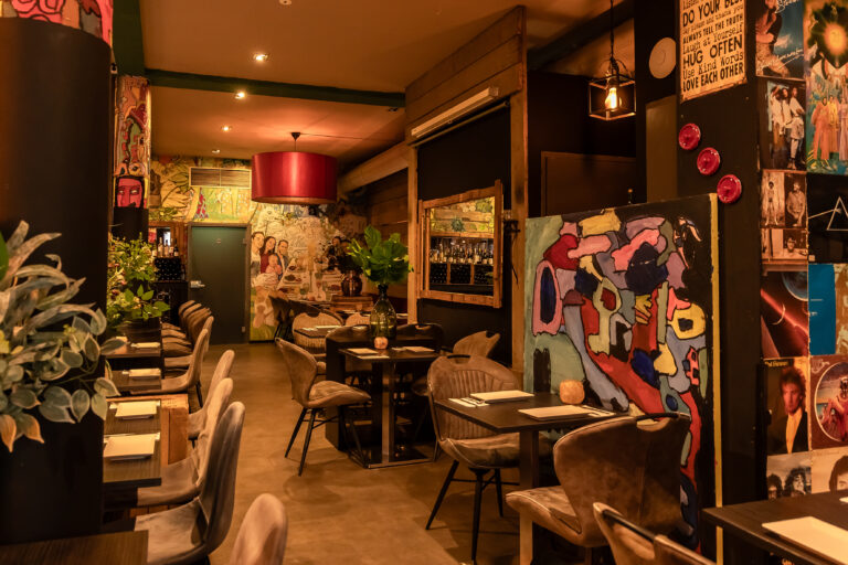 Sfeervol restaurantinterieur met eclectische kunst aan de muren, ingerichte tafels en warme verlichting.