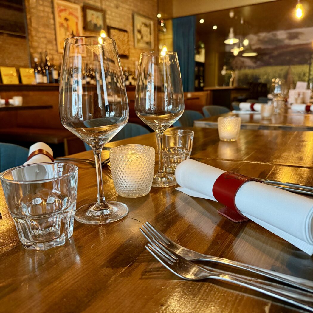Restaurant tafelschikking: houten tafel, wijnglazen, bestek, servetten, kaarsjes.