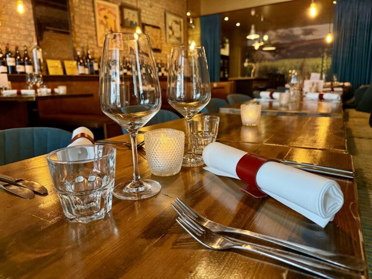Restaurant tafelschikking: houten tafel, wijnglazen, bestek, servetten, kaarsjes.