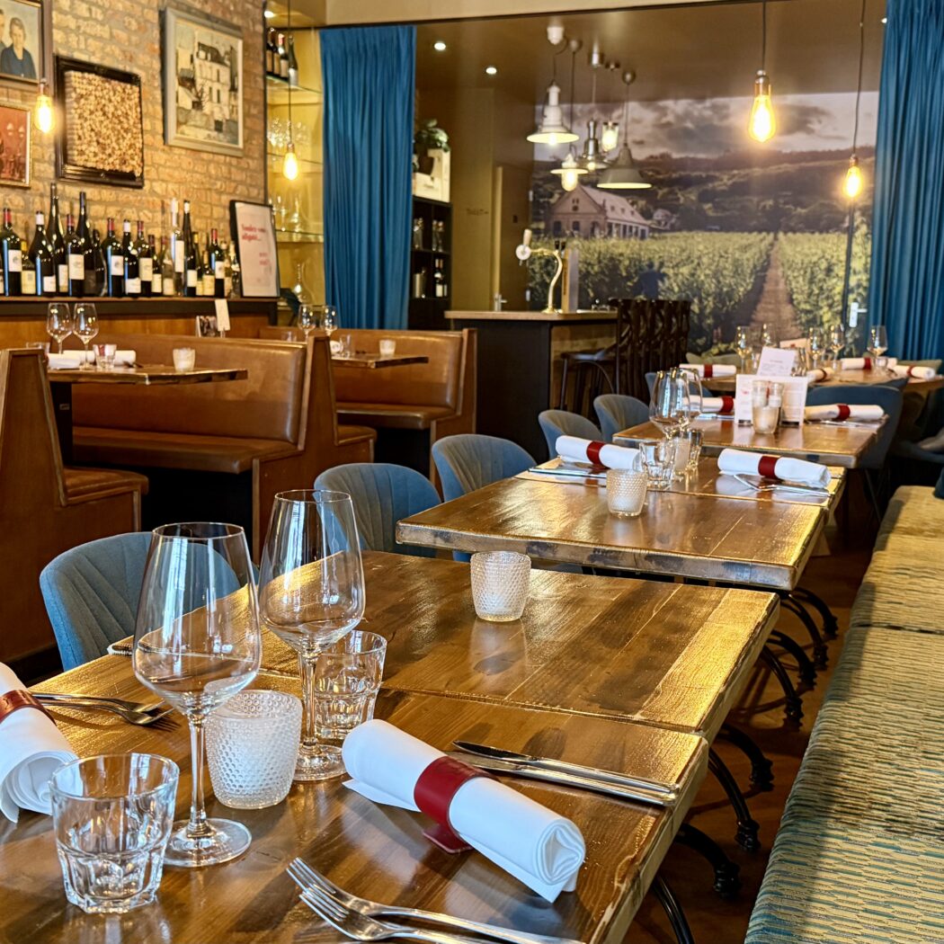Restaurant interieur: houten tafels, stoelen en banken, wijnrek met flessen.