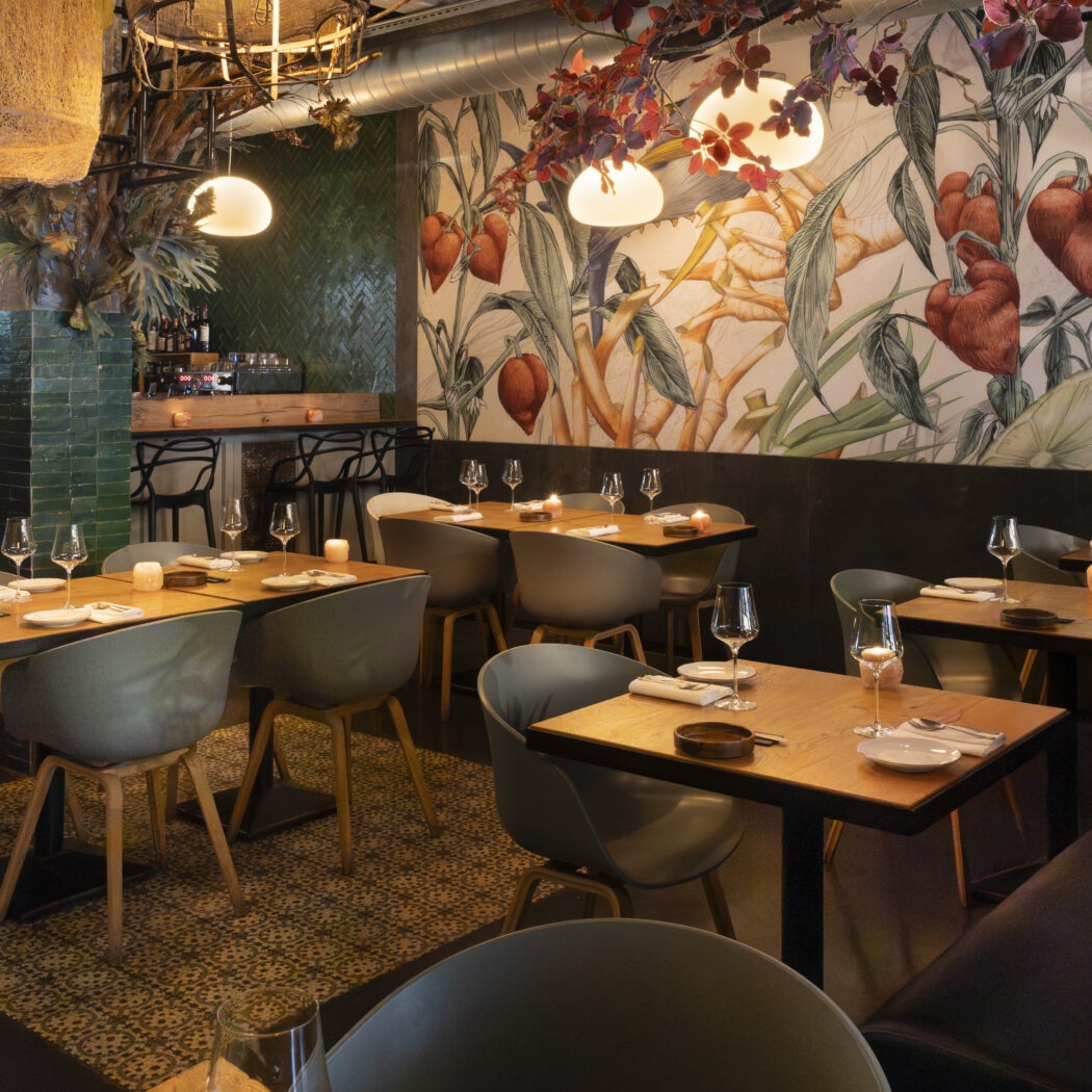 Modern restaurantinterieur met houten tafels, grijze stoelen, een bar en een kleurrijke muurschildering van planten en een varken.