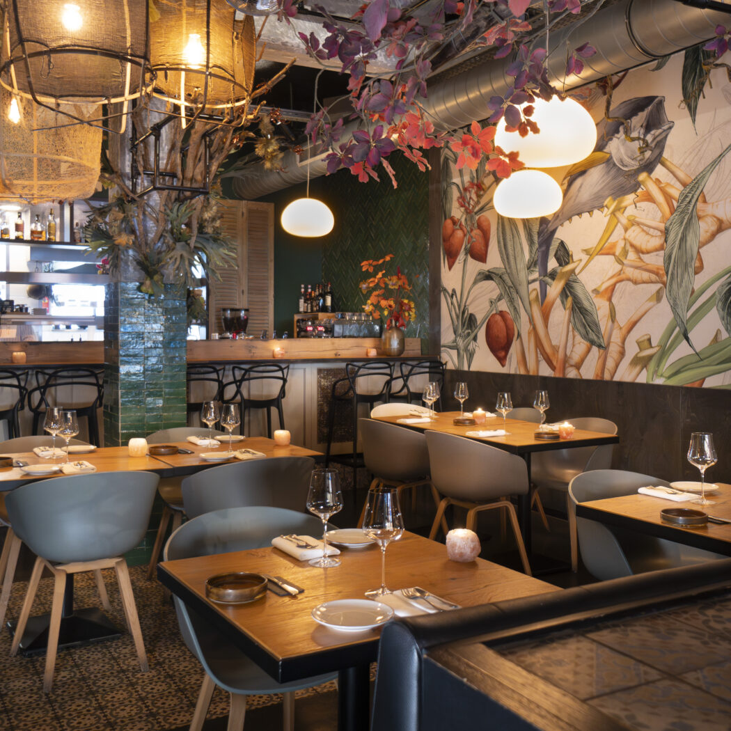 Sfeervol restaurantinterieur met houten tafels, moderne stoelen, een bar en een grote jungle muurschildering.