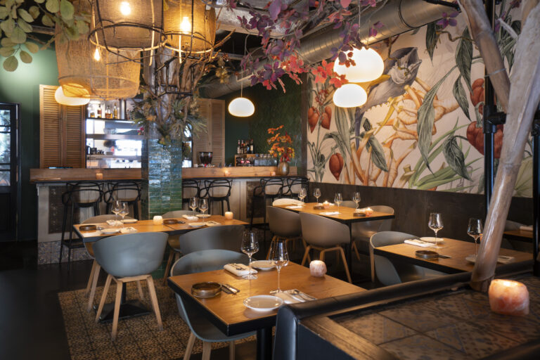 Sfeervol restaurantinterieur met houten tafels, moderne stoelen, een bar en een grote jungle muurschildering.