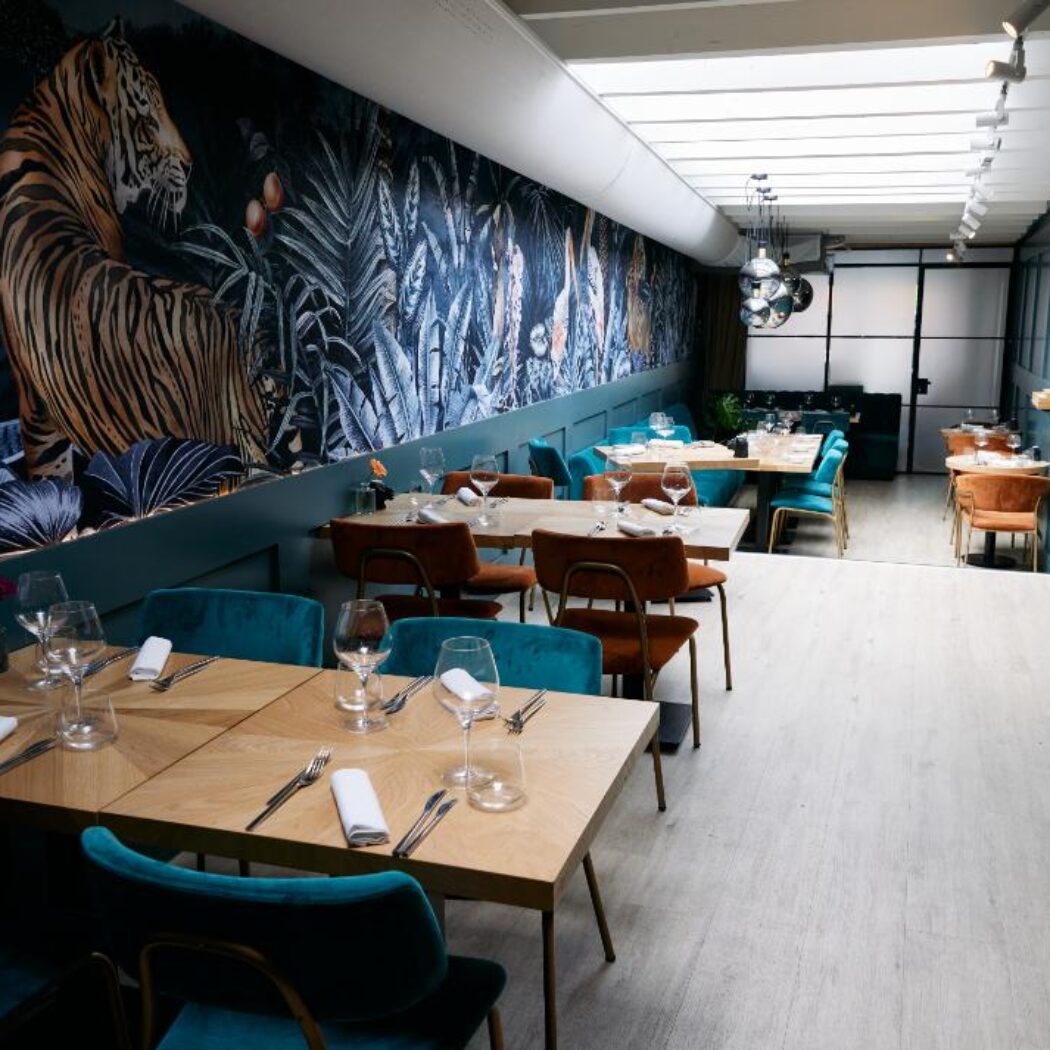 Sfeervol restaurant met opvallend tijgerbehang, gedekte houten tafels en blauwgroene en terracotta stoelen.