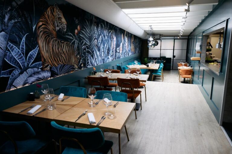 Sfeervol restaurant met opvallend tijgerbehang, gedekte houten tafels en blauwgroene en terracotta stoelen.
