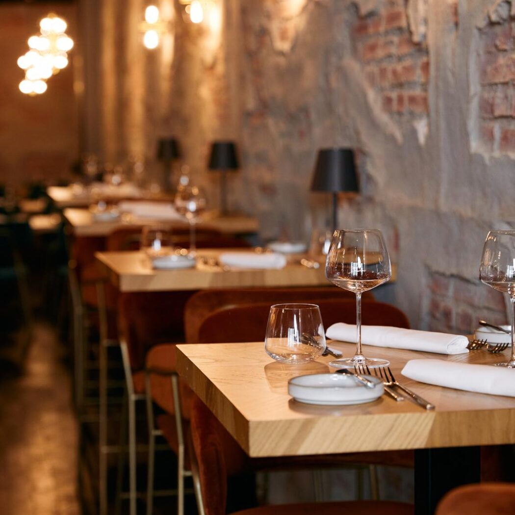 Gezellig restaurant interieur met houten tafels, oranje stoelen, industriële bakstenen muur en warme sfeerverlichting.