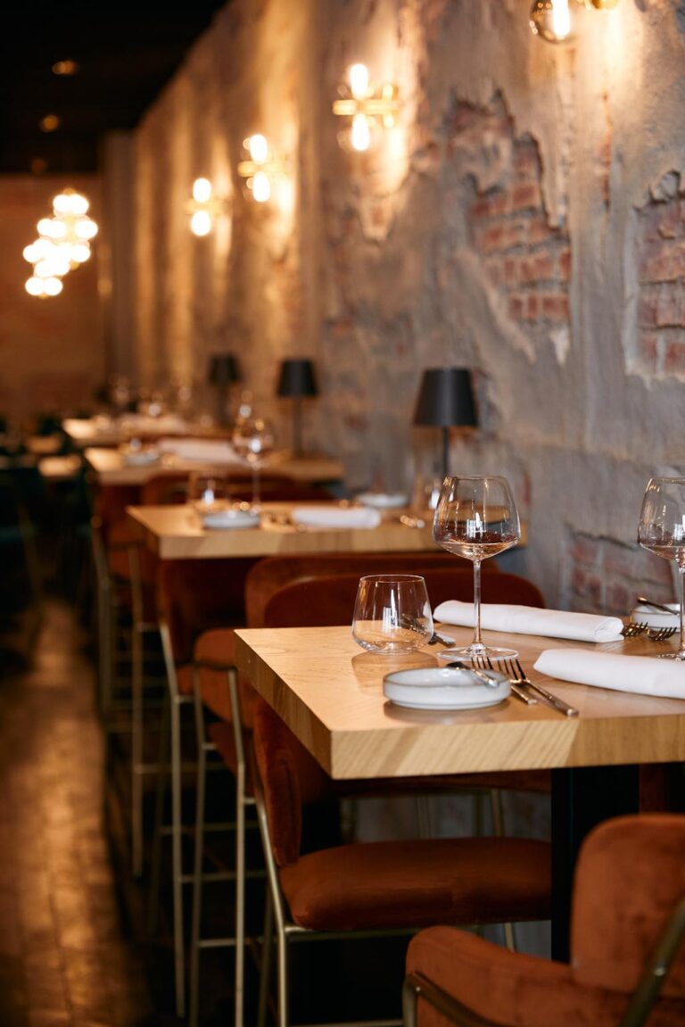 Gezellig restaurant interieur met houten tafels, oranje stoelen, industriële bakstenen muur en warme sfeerverlichting.