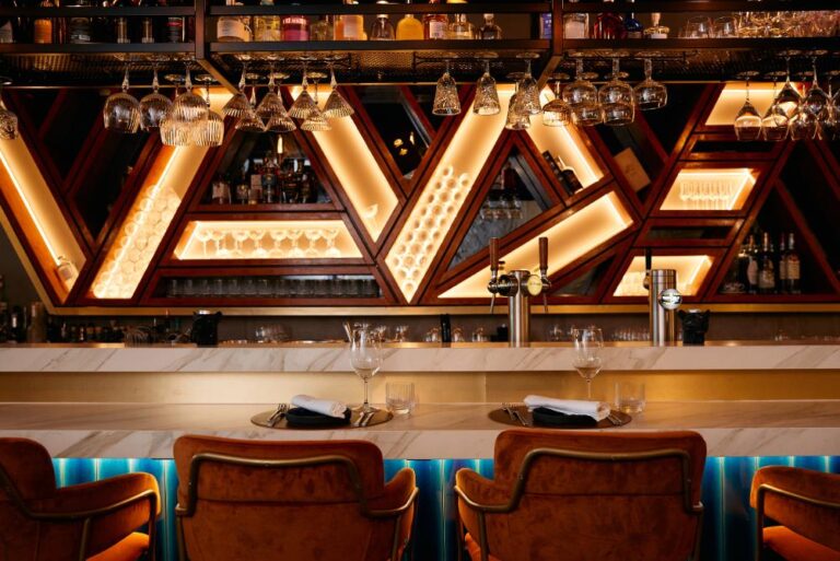 Luxe bar interieur met marmeren toonbank, oranje fluwelen barkrukken en geometrische verlichte drankrekken.