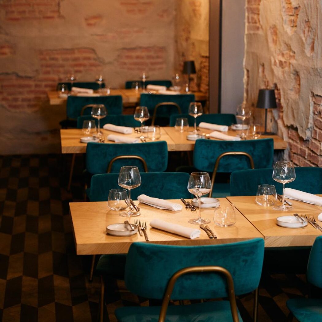 Sfeervol restaurantinterieur met gedekte houten tafels, teal fluwelen stoelen en bakstenen muren.