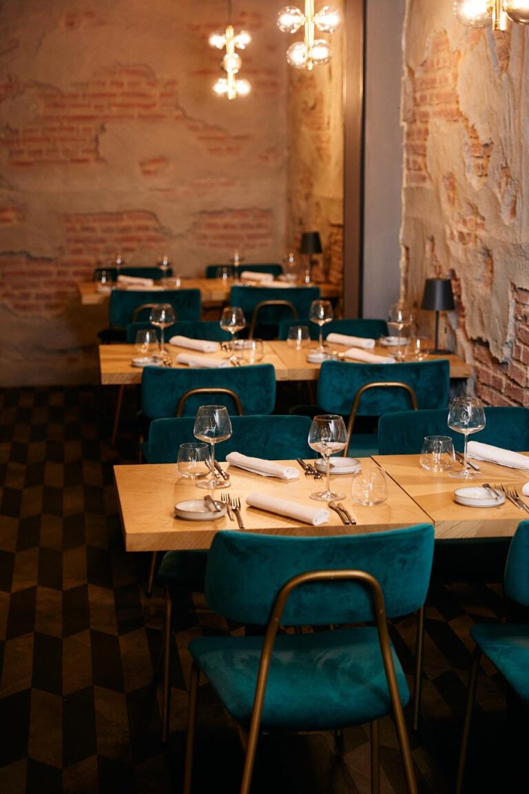 Sfeervol restaurantinterieur met gedekte houten tafels, teal fluwelen stoelen en bakstenen muren.