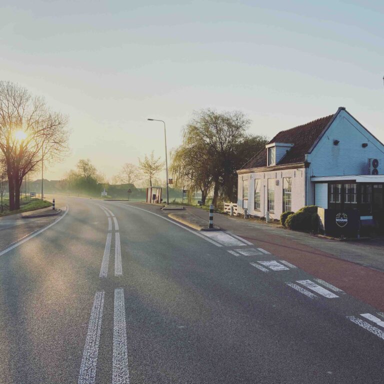 Stille landelijke weg bij zonsopgang, met wit huis met rood dak en SCHANS uithangbord.