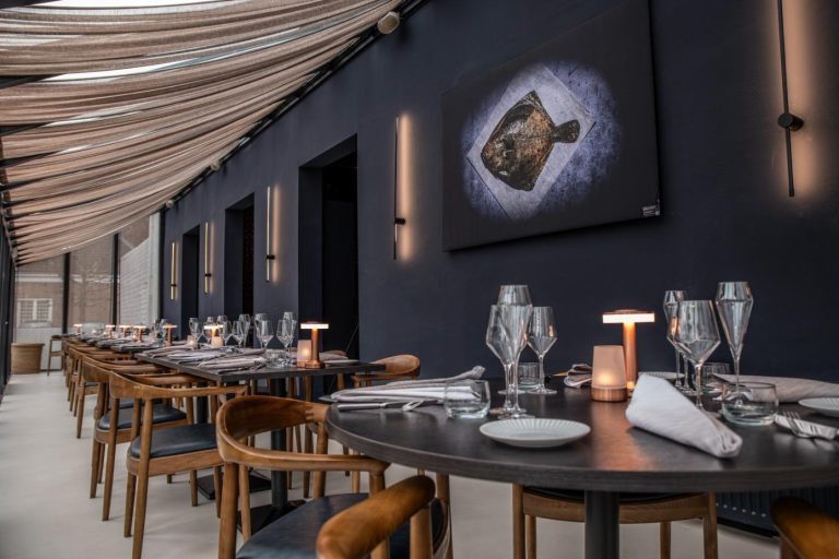 Stijlvol restaurantinterieur met donkere muren, gedrapeerd plafond en gedekte tafels met viskunst.