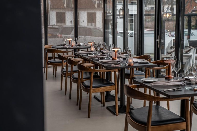 Moderne restaurantruimte met rijen gedekte zwarte tafels, houten stoelen en grote ramen.