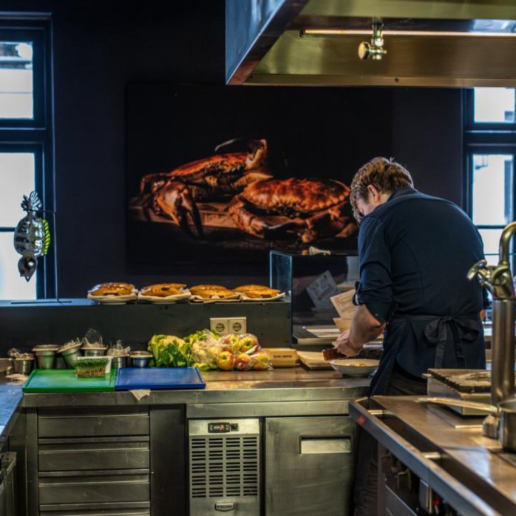 Chef bereidt maaltijden in een professionele keuken, met bereide gerechten en een grote afbeelding van krabben.