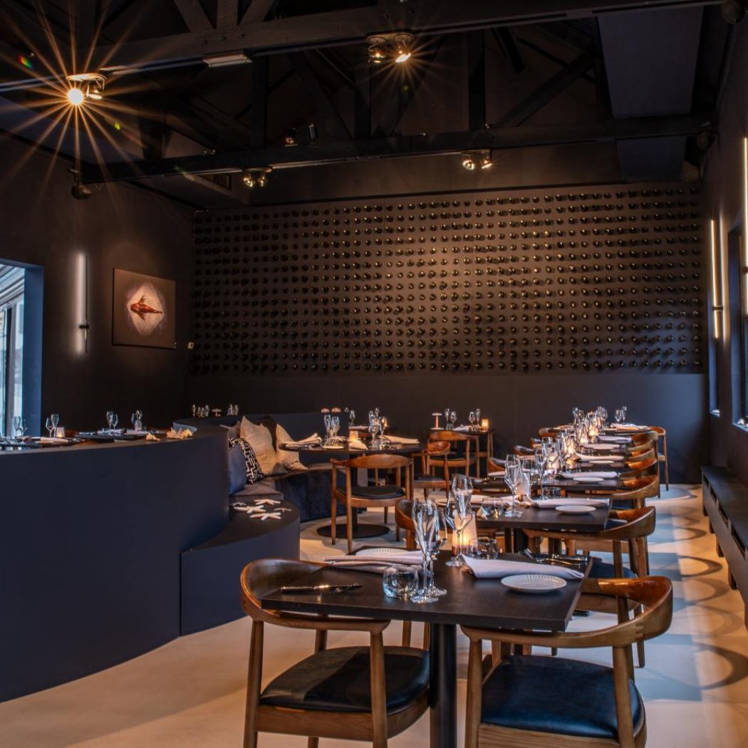Chic restaurant interieur met donkere muren, gedekte tafels, houten stoelen en een wijnflessenmuur.