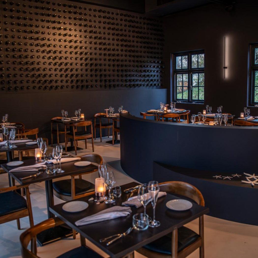 Elegant restaurantinterieur met wijnwand, gedekte tafels, kaarslicht en een gebogen bank met zeesterren.