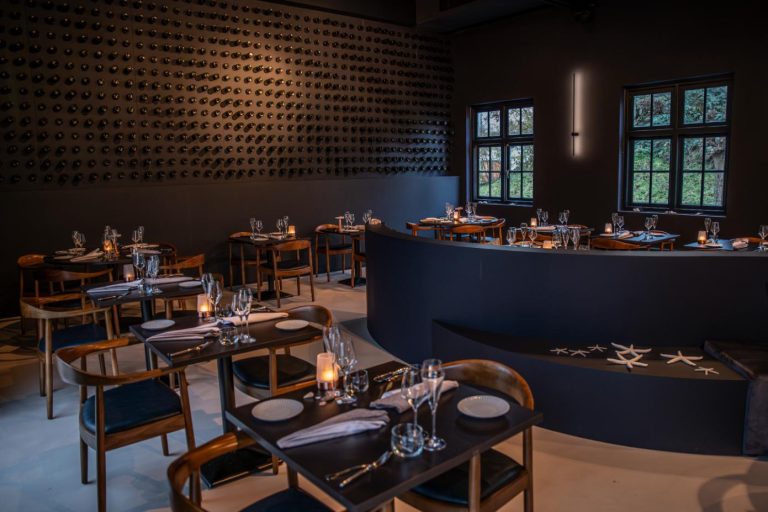 Elegant restaurantinterieur met wijnwand, gedekte tafels, kaarslicht en een gebogen bank met zeesterren.