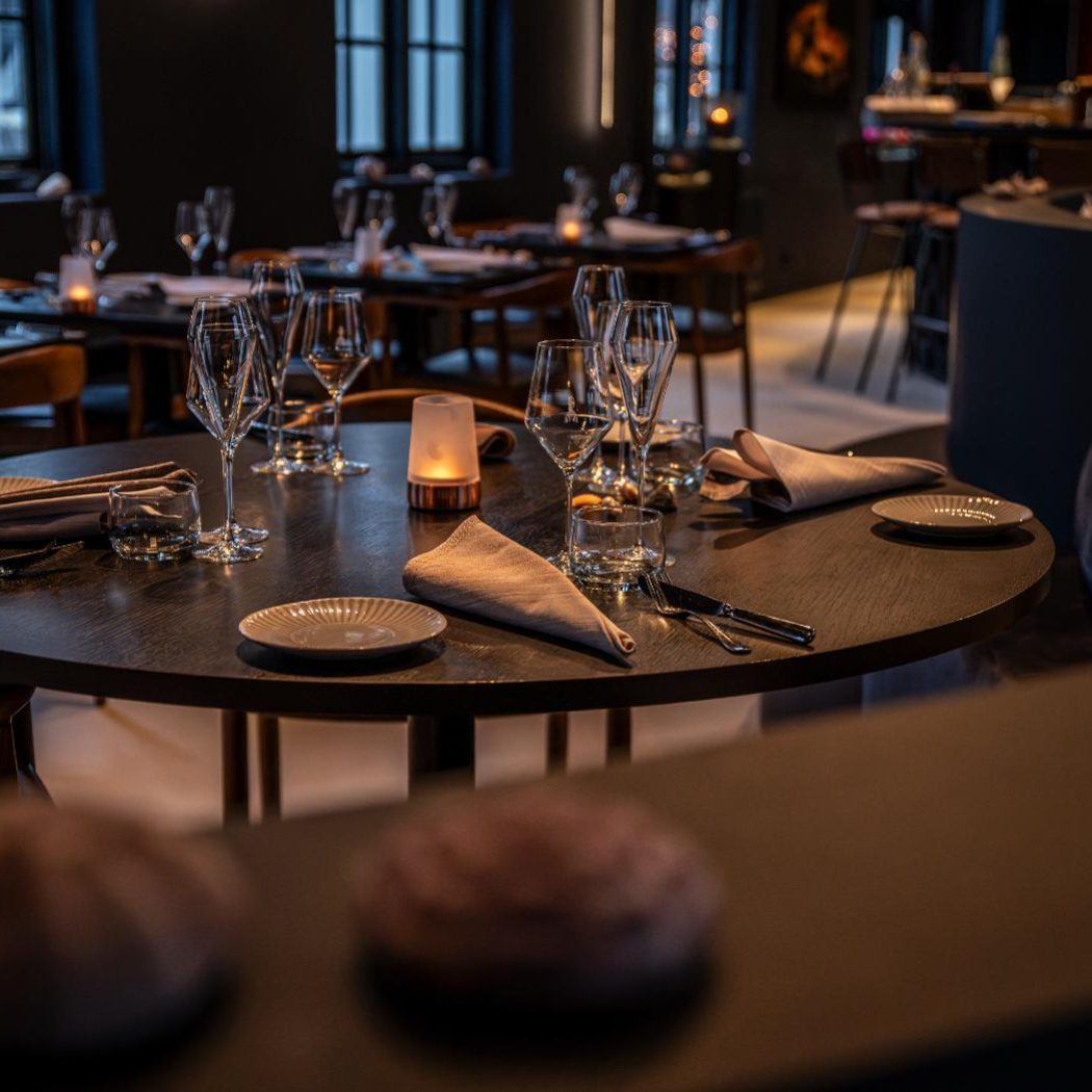 Sfeervol gedekte ronde houten tafel in een modern restaurant met glazen, borden, bestek en een kaars.
