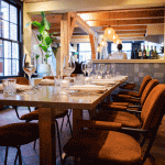 Atmospheric restaurant table with wine glasses, white napkins and rust-brown velvet chairs.