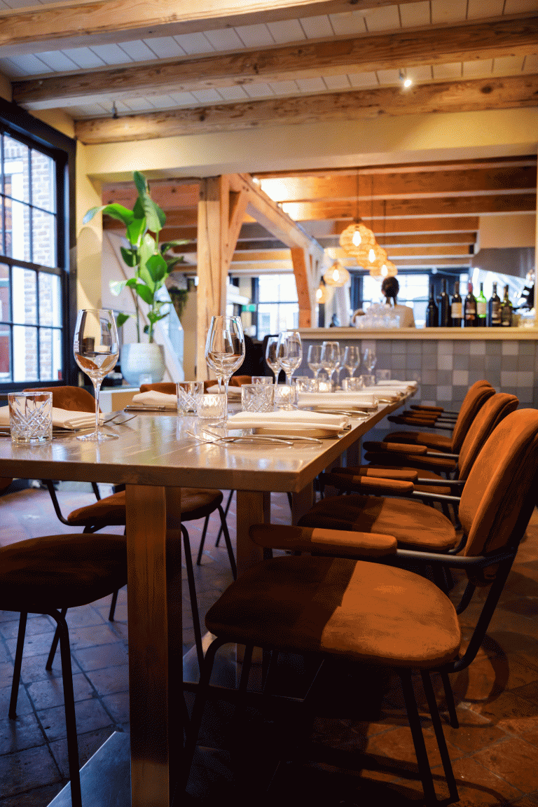 Sfeervolle restauranttafel met wijnglazen, witte servetten en roestbruine fluwelen stoelen.